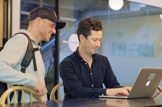 Two people smiling and working on a laptop in an office space.