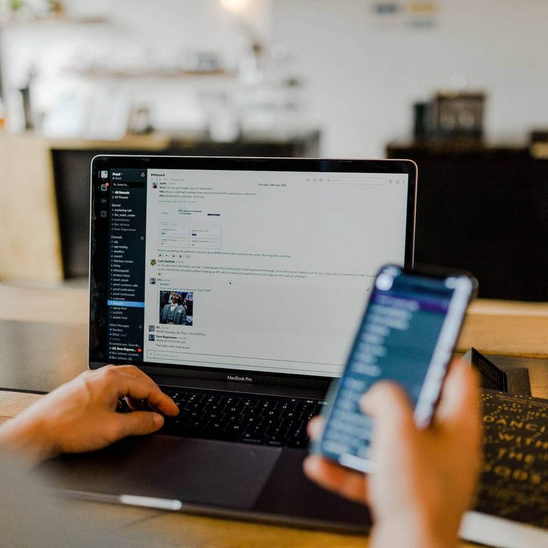 Point-of-view of a person looking at a phone screen and a laptop open to a work Slack channel.